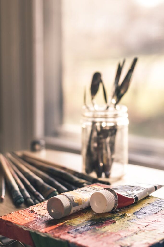 pexels-photo-1055077 Close-up of paint tubes and brushes on a table by the window in warm lighting. Perfect for creative themes.